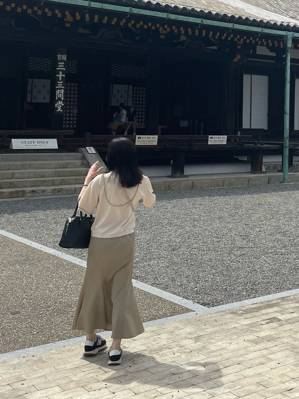 ブラック系のスニーカー、ベージュ系のスカート、ブラック系のショルダーバッグを着用したレディースの夏コーディネートの2枚目の写真