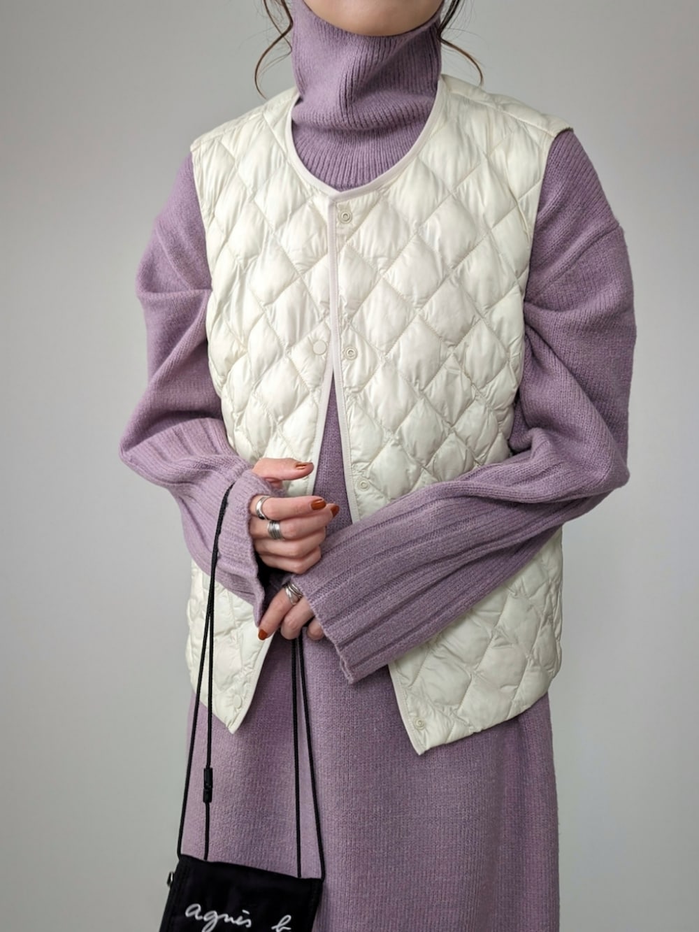 パープル系のワンピース、ブラック系のパンプス、ホワイト系のベストを着用したレディースの冬コーディネートの2枚目の写真