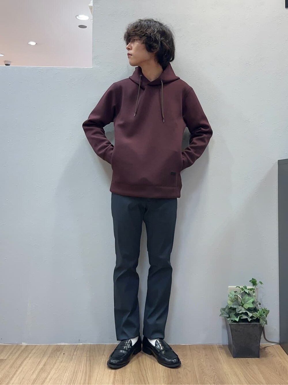 レッド系のパーカー、ブラック系のスラックス、ブルー系のクラッチバッグを着用したメンズの秋コーディネートの3枚目の写真