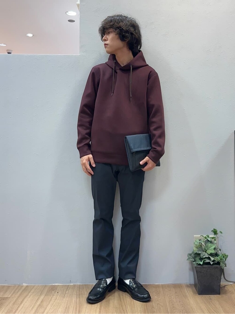 レッド系のパーカー、ブラック系のスラックス、ブルー系のクラッチバッグを着用したメンズの秋コーディネートの2枚目の写真