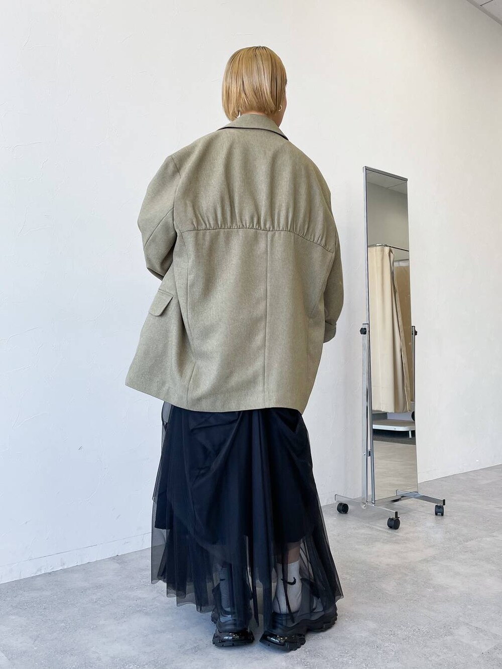 グリーン系のテーラードジャケット、ブラック系のスカート、グレー系のサンダルを着用したレディースの春コーディネートの3枚目の写真