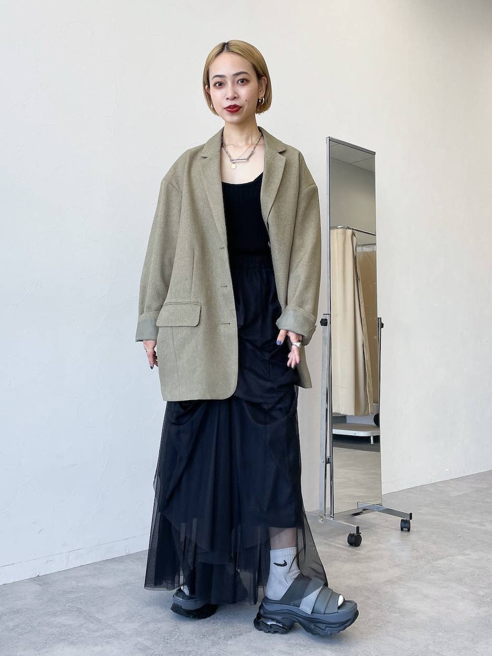 グリーン系のテーラードジャケット、ブラック系のスカート、グレー系のサンダルを着用したレディースの春コーディネートの2枚目の写真