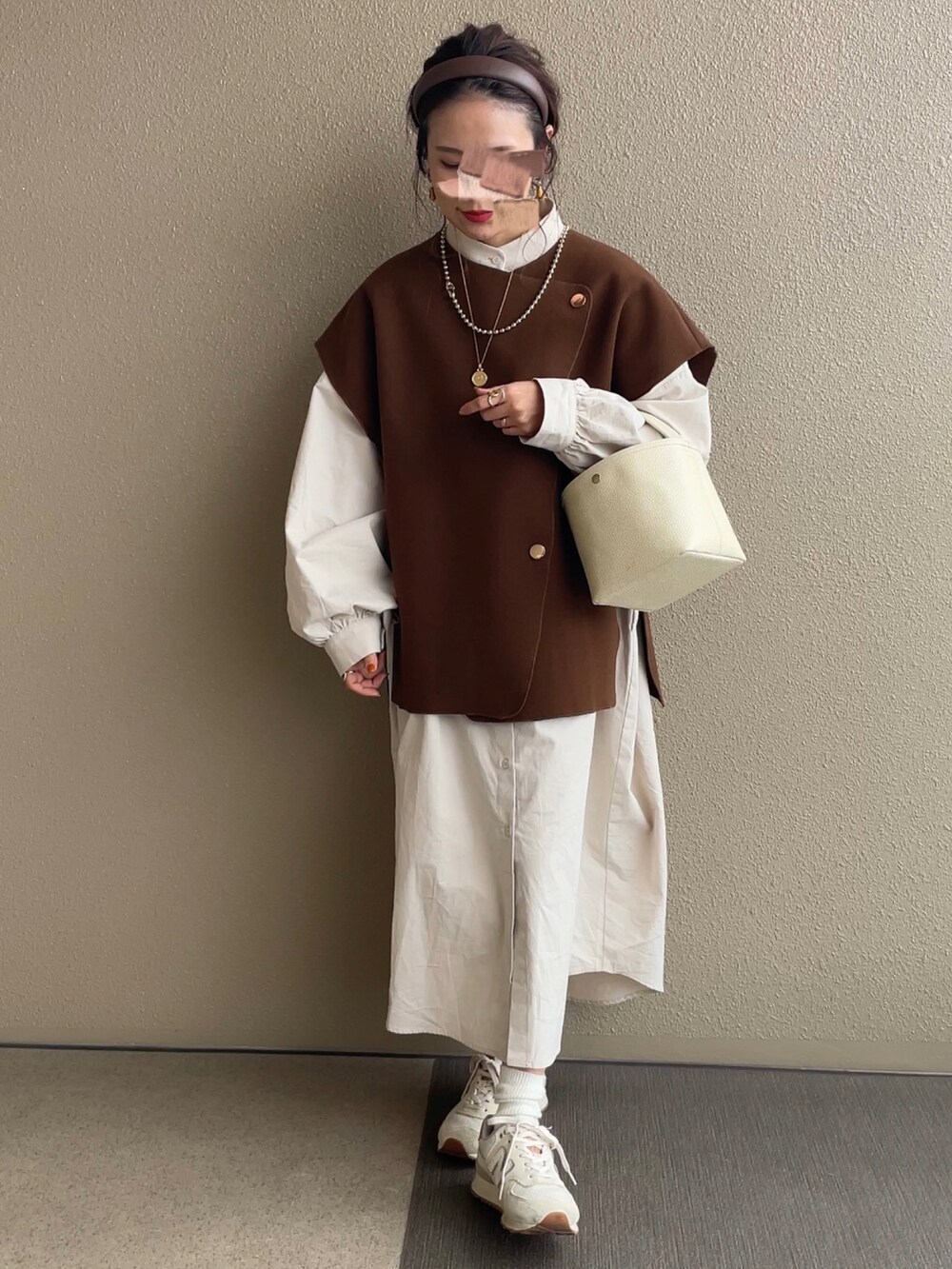 ホワイト系のワンピース、ブラウン系のベスト、ベージュ系のスニーカーを着用したレディースの秋コーディネートの2枚目の写真
