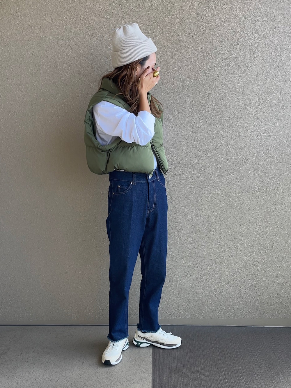 グリーン系のベスト、ブルー系のデニムパンツ、ベージュ系のスニーカーを着用したレディースの秋コーディネートの2枚目の写真