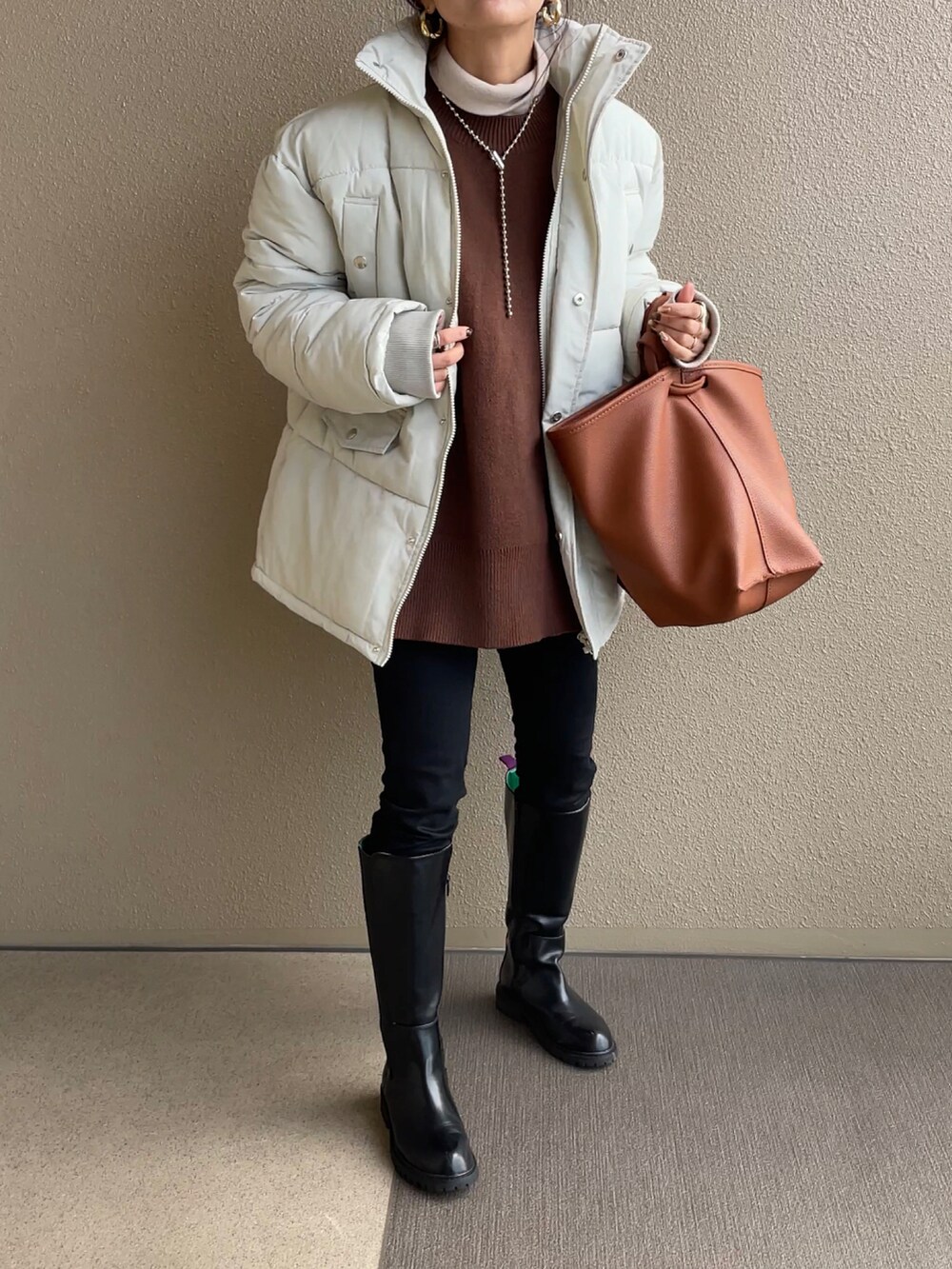 ホワイト系のダウンジャケット/コート、ブラック系のブーツ、ブラウン系のバッグを着用したレディースの冬コーディネートの2枚目の写真
