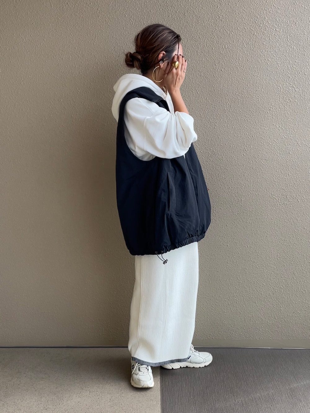 ホワイト系のパーカー、ホワイト系のスカート、ブラック系のベストを着用したレディースの秋コーディネートの4枚目の写真