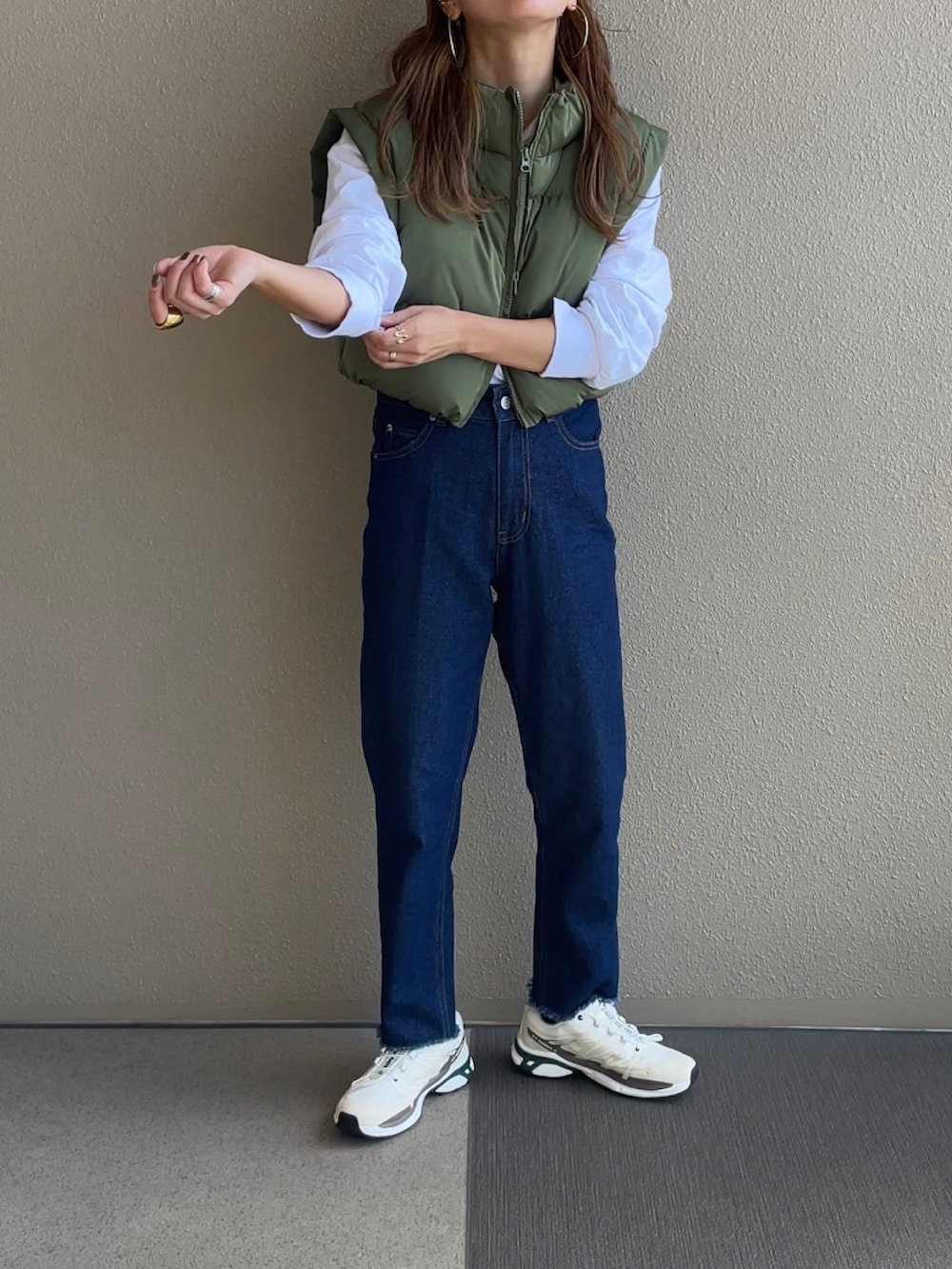 グリーン系のベスト、ブルー系のデニムパンツ、ベージュ系のスニーカーを着用したレディースの秋コーディネートの3枚目の写真