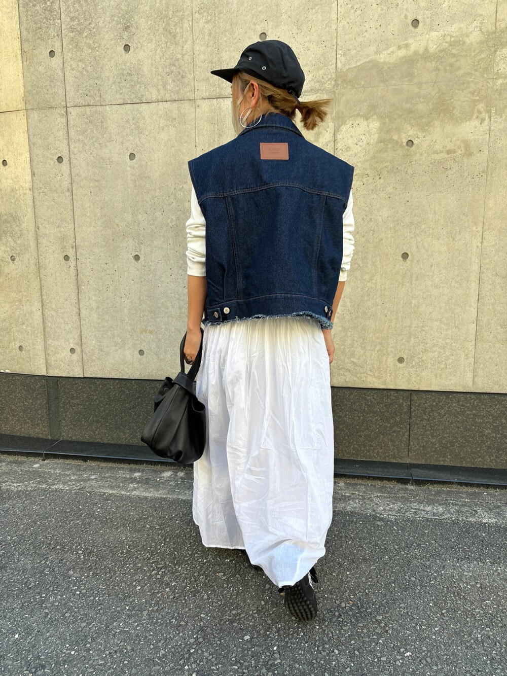 ブルー系のベスト、ホワイト系のワンピース、ブラック系のキャップを着用したレディースの春コーディネートの5枚目の写真