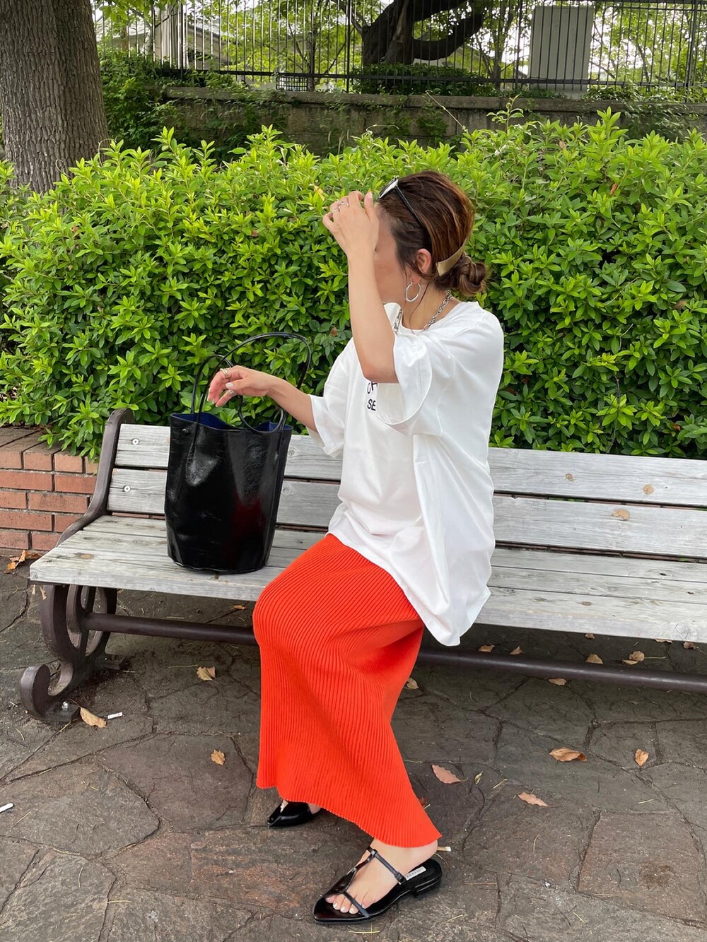 ホワイト系のTシャツ/カットソー、オレンジ系のスカート、ブラック系のショルダーバッグを着用したレディースの夏コーディネートの2枚目の写真