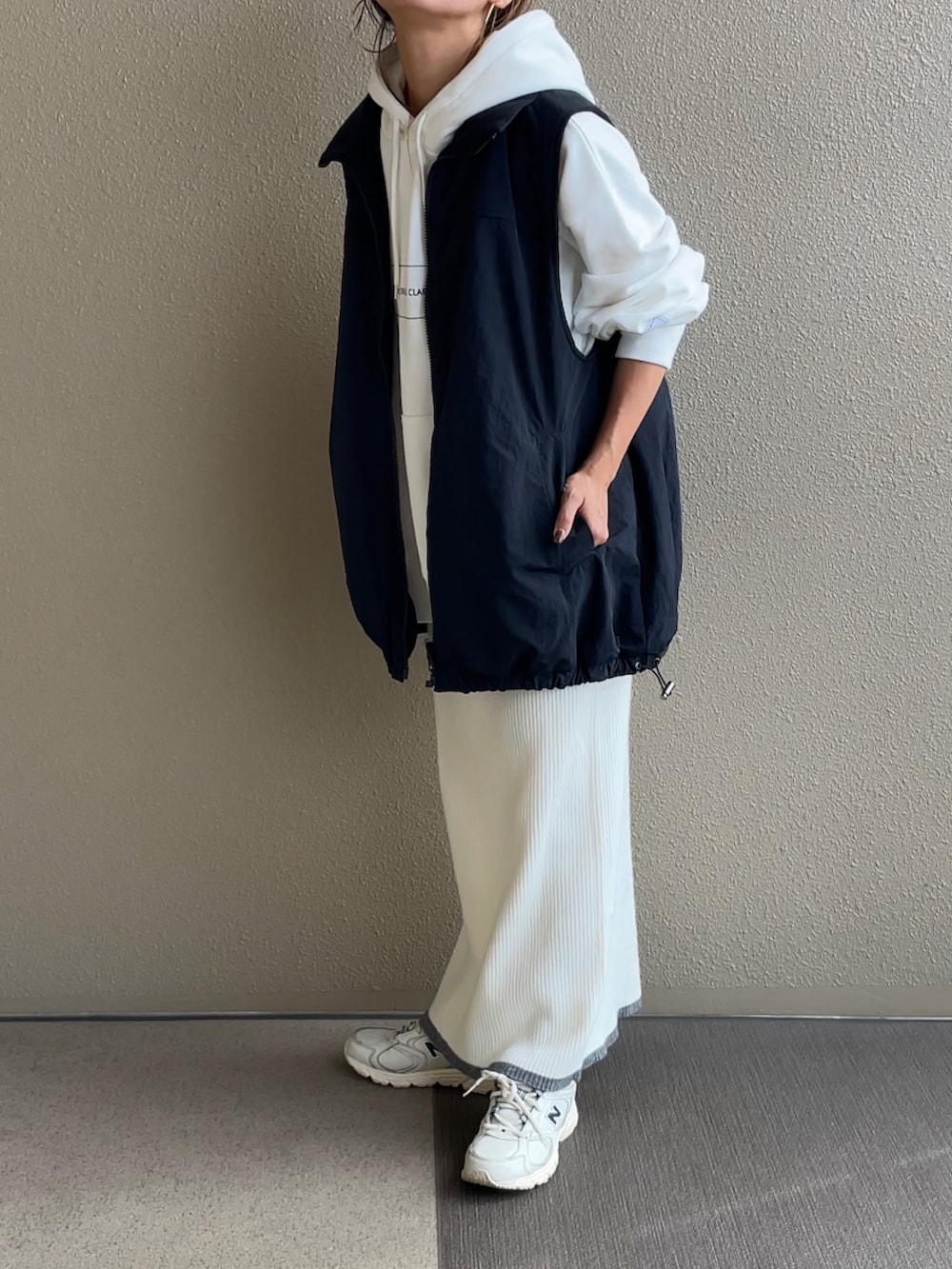 ホワイト系のパーカー、ホワイト系のスカート、ブラック系のベストを着用したレディースの秋コーディネートの3枚目の写真