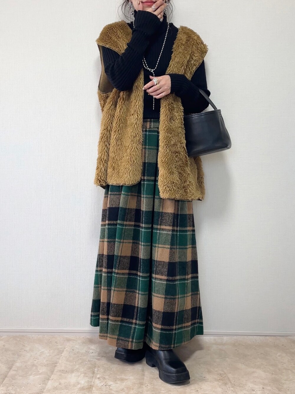 グリーン系のスカート、ブラウン系のベスト、ブラック系のその他アウターを着用したレディースの冬コーディネートの2枚目の写真