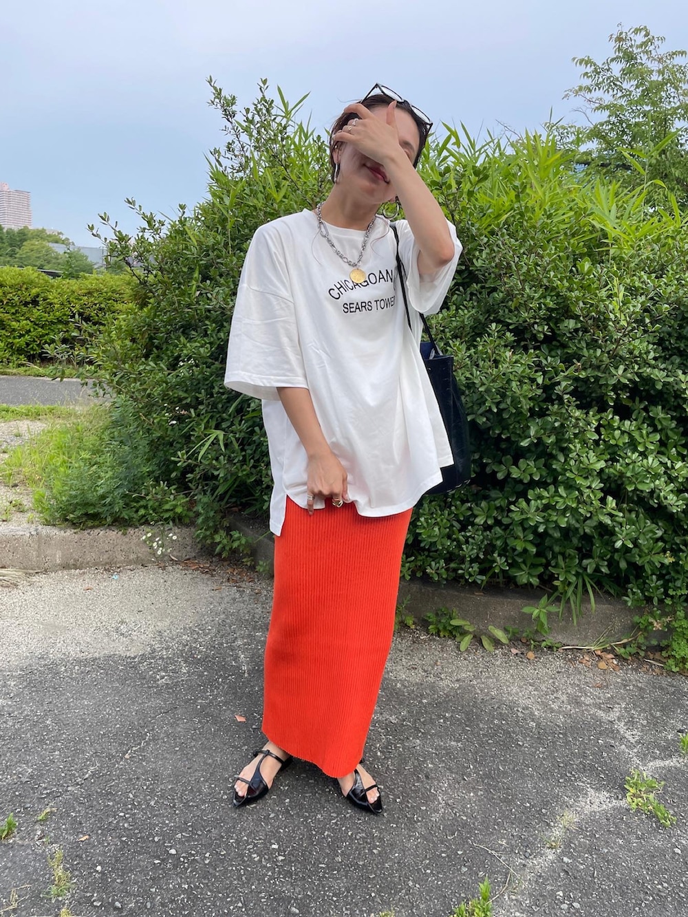 ホワイト系のTシャツ/カットソー、オレンジ系のスカート、ブラック系のショルダーバッグを着用したレディースの夏コーディネートの3枚目の写真