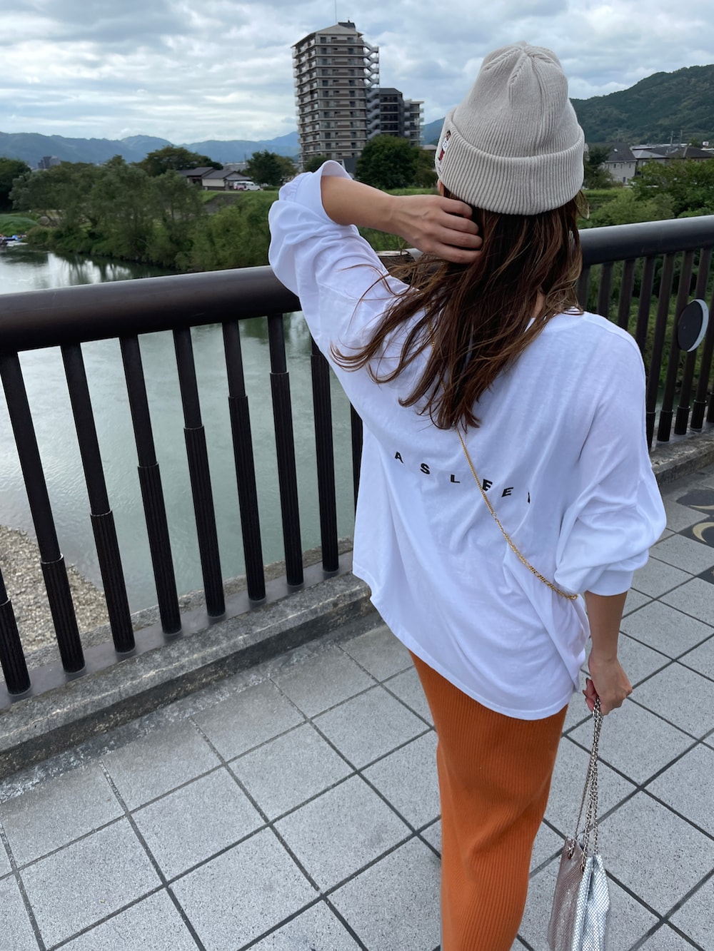 オレンジ系のスカート、ホワイト系のTシャツ/カットソー、シルバー系のショルダーバッグを着用したレディースの秋コーディネートの3枚目の写真