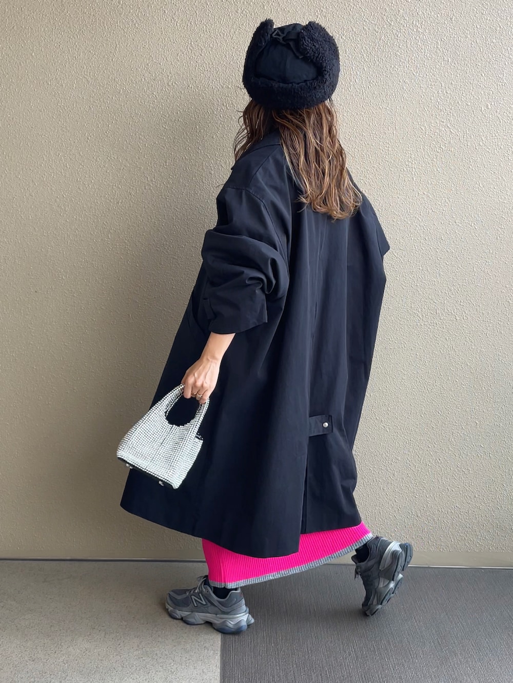 ブラック系のニット/セーター、ブラック系のステンカラーコート、ピンク系のスカートを着用したレディースの秋コーディネートの2枚目の写真