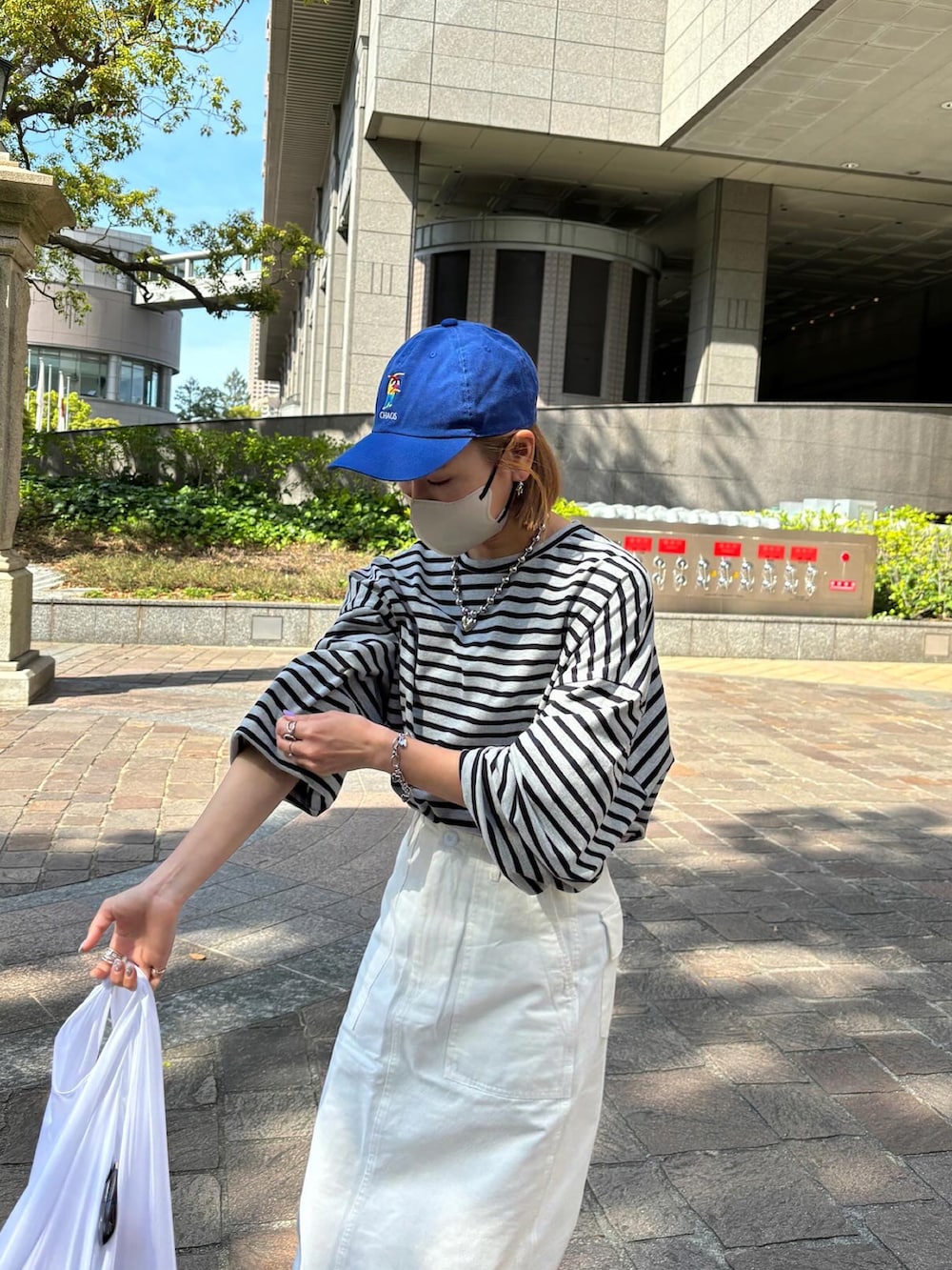 グレー系のTシャツ/カットソー、ホワイト系のスカート、ブラック系のナイロンジャケットを着用したレディースの春コーディネートの2枚目の写真