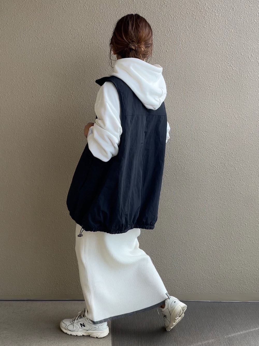 ホワイト系のパーカー、ホワイト系のスカート、ブラック系のベストを着用したレディースの秋コーディネートの2枚目の写真