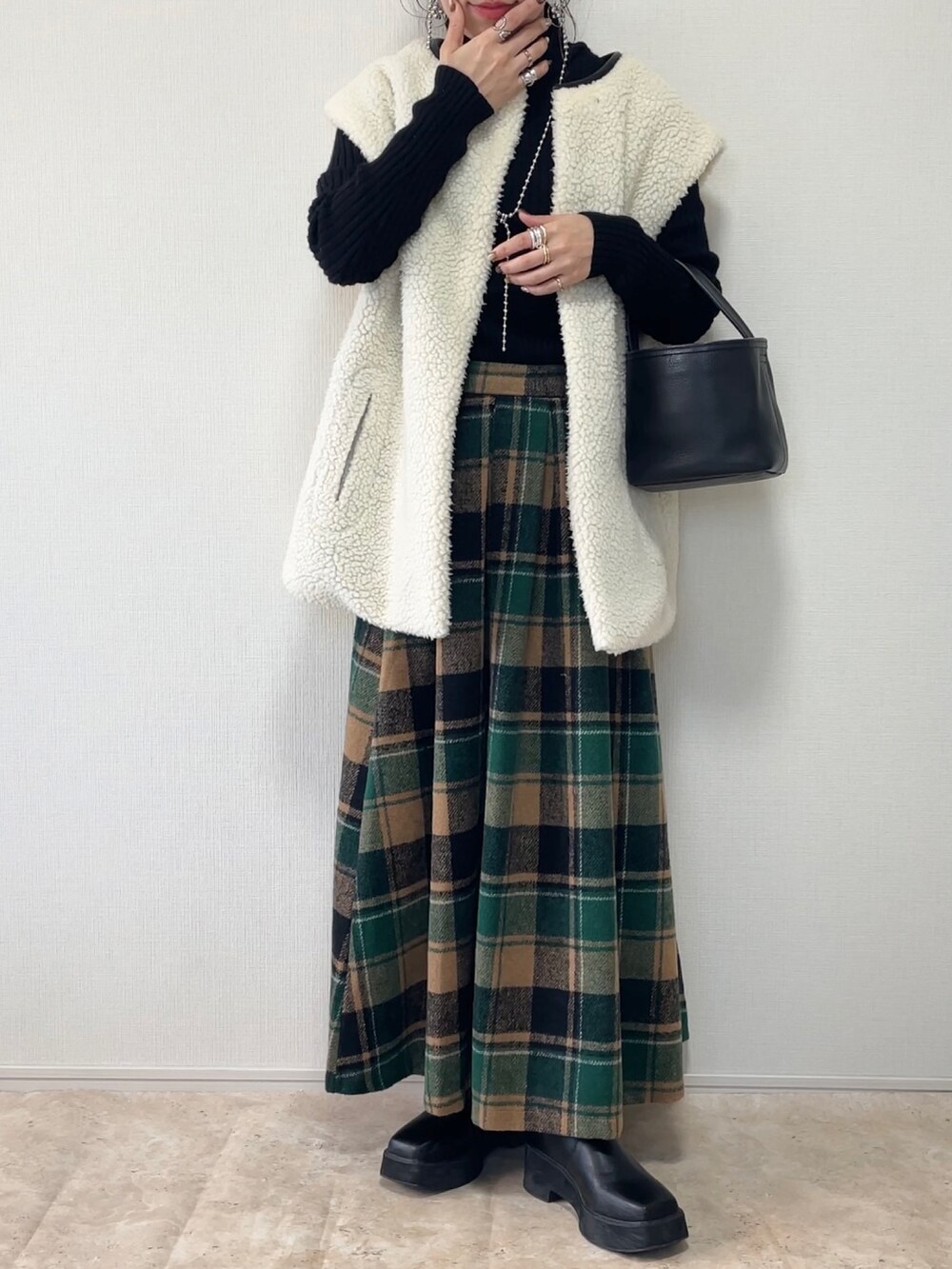 グリーン系のスカート、ブラウン系のベスト、ブラック系のその他アウターを着用したレディースの冬コーディネートの3枚目の写真