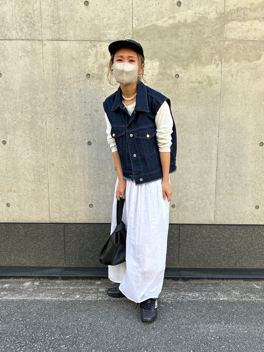 ブルー系のベスト、ホワイト系のワンピース、ブラック系のキャップを着用したレディースの春コーディネートの2枚目の写真