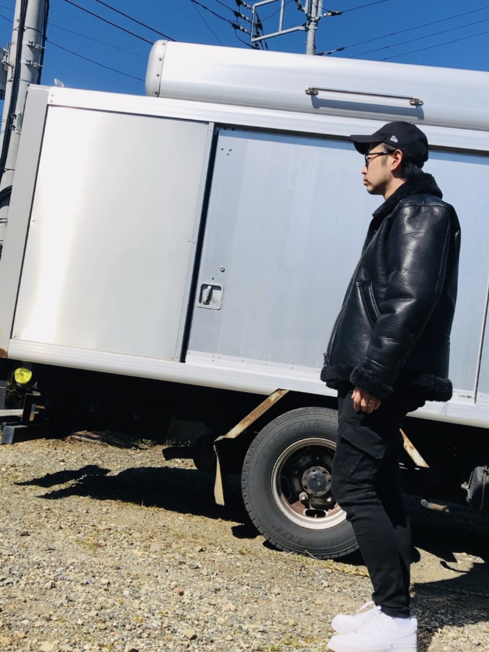 ブラック系のライダースジャケット、ブラック系のカーゴパンツ、ホワイト系のスニーカーを着用したメンズの春コーディネートの2枚目の写真