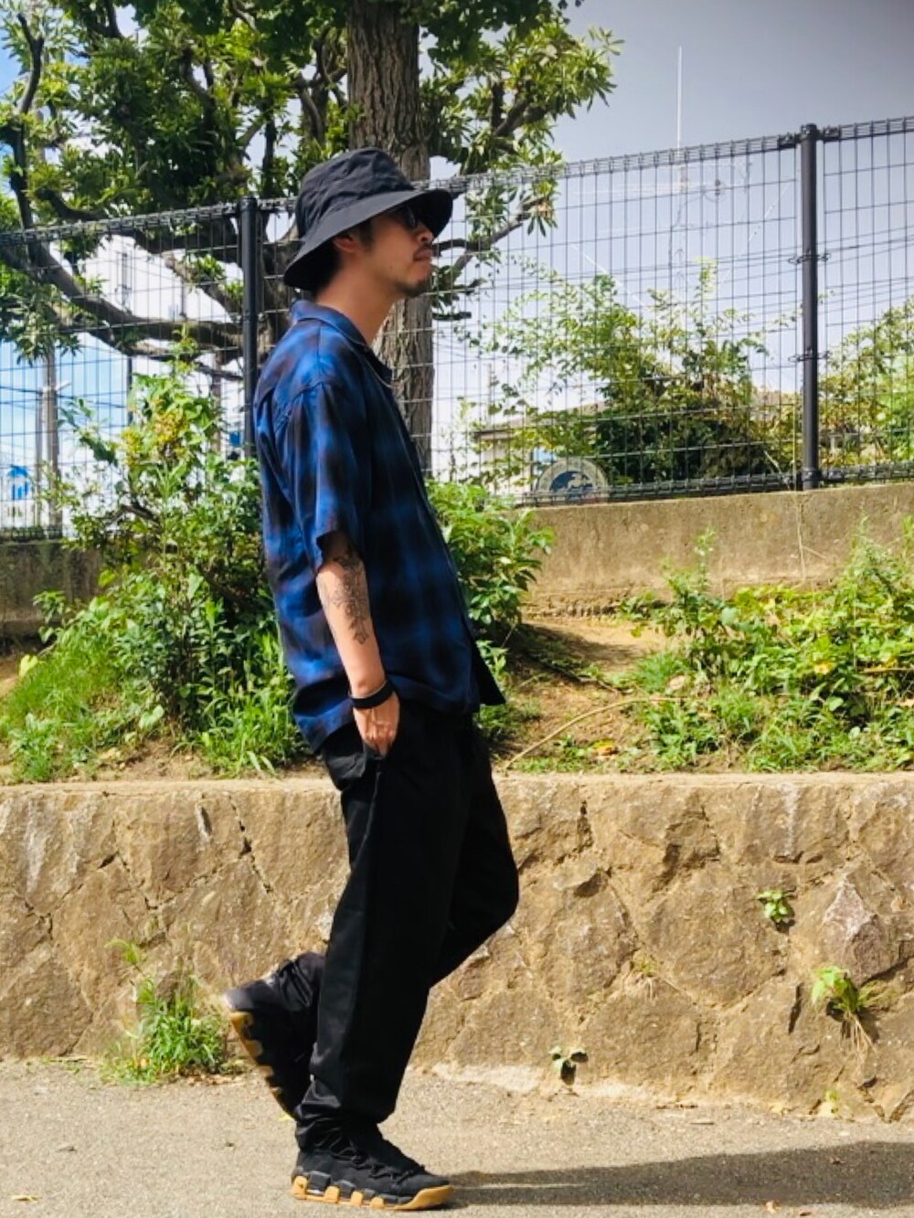 ブルー系のトップス、ブラック系のスニーカー、ブラック系のチノパンツを着用したメンズの夏コーディネートの3枚目の写真