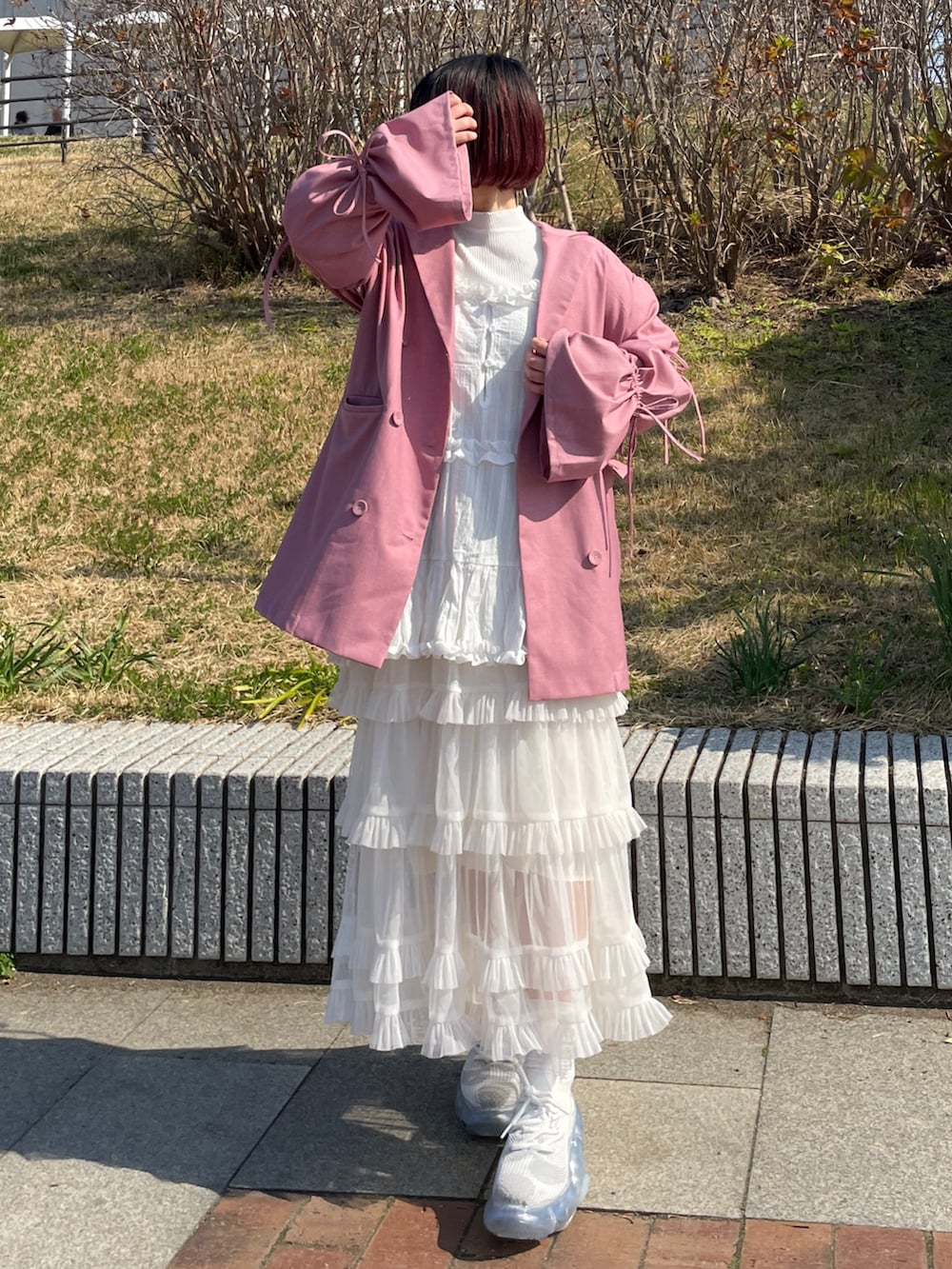 ピンク系のテーラードジャケット、ホワイト系のハンドバッグ、ホワイト系のスニーカーを着用したレディースの春コーディネートの2枚目の写真