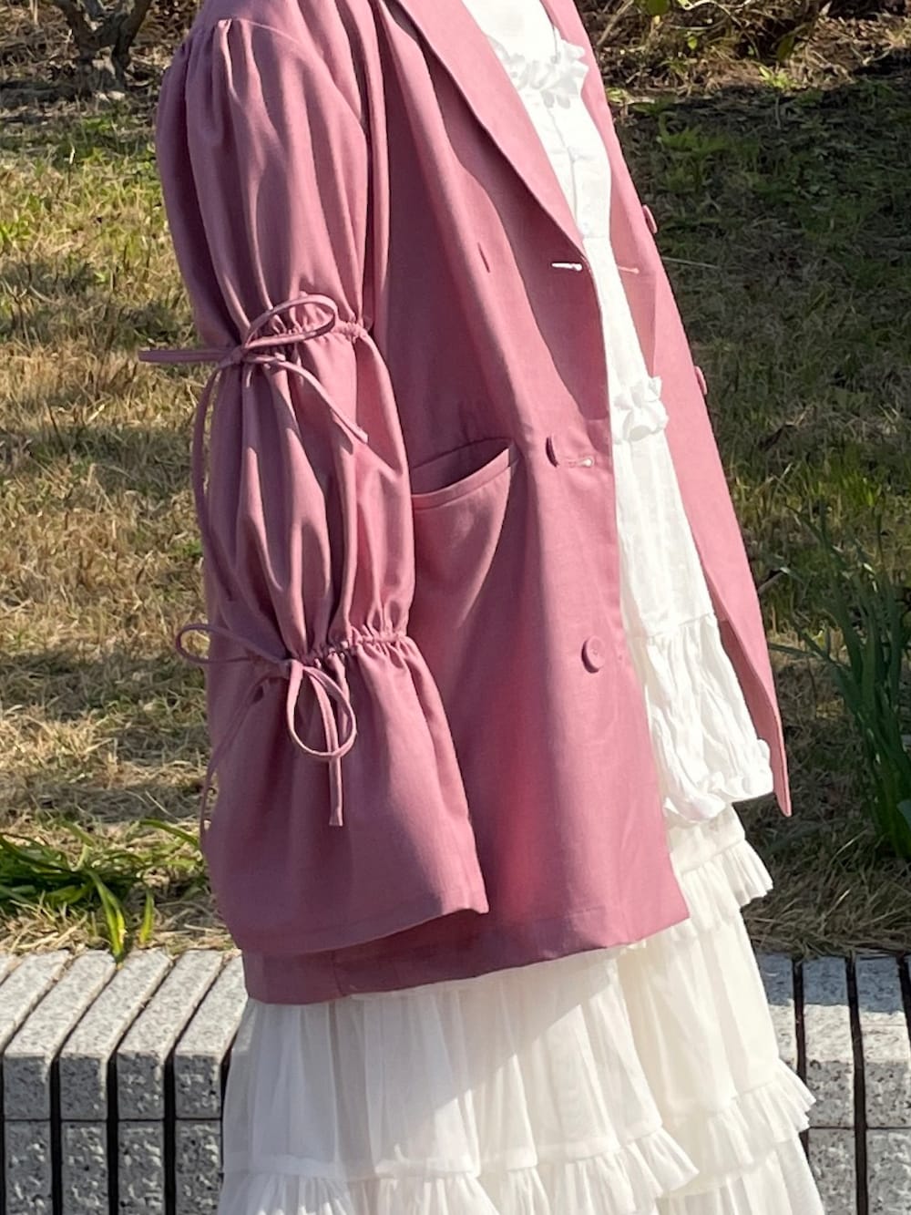 ピンク系のテーラードジャケット、ホワイト系のハンドバッグ、ホワイト系のスニーカーを着用したレディースの春コーディネートの5枚目の写真