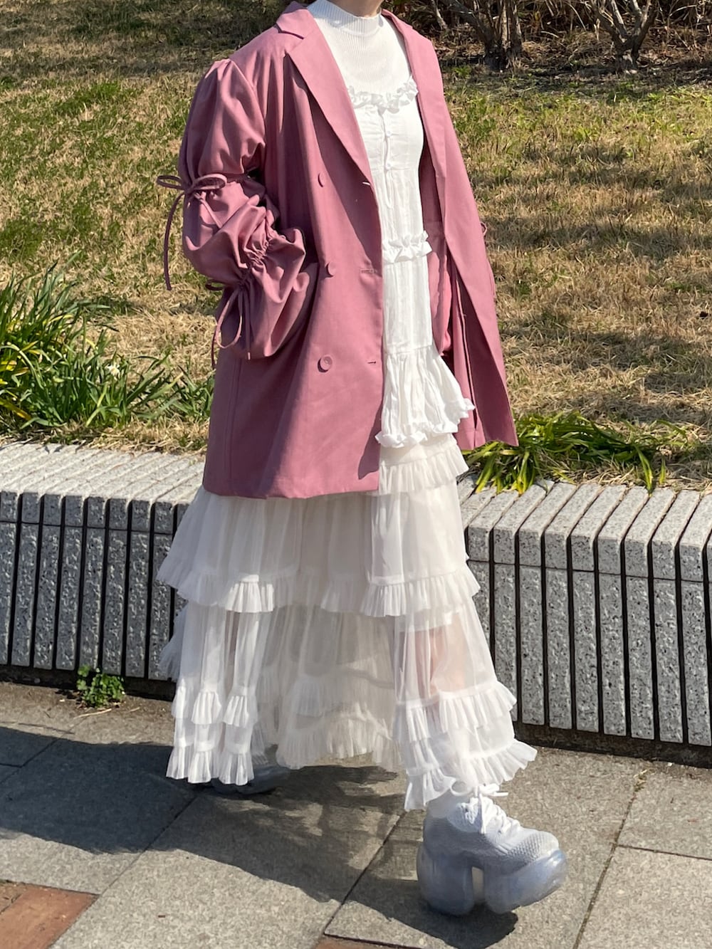 ピンク系のテーラードジャケット、ホワイト系のハンドバッグ、ホワイト系のスニーカーを着用したレディースの春コーディネートの4枚目の写真