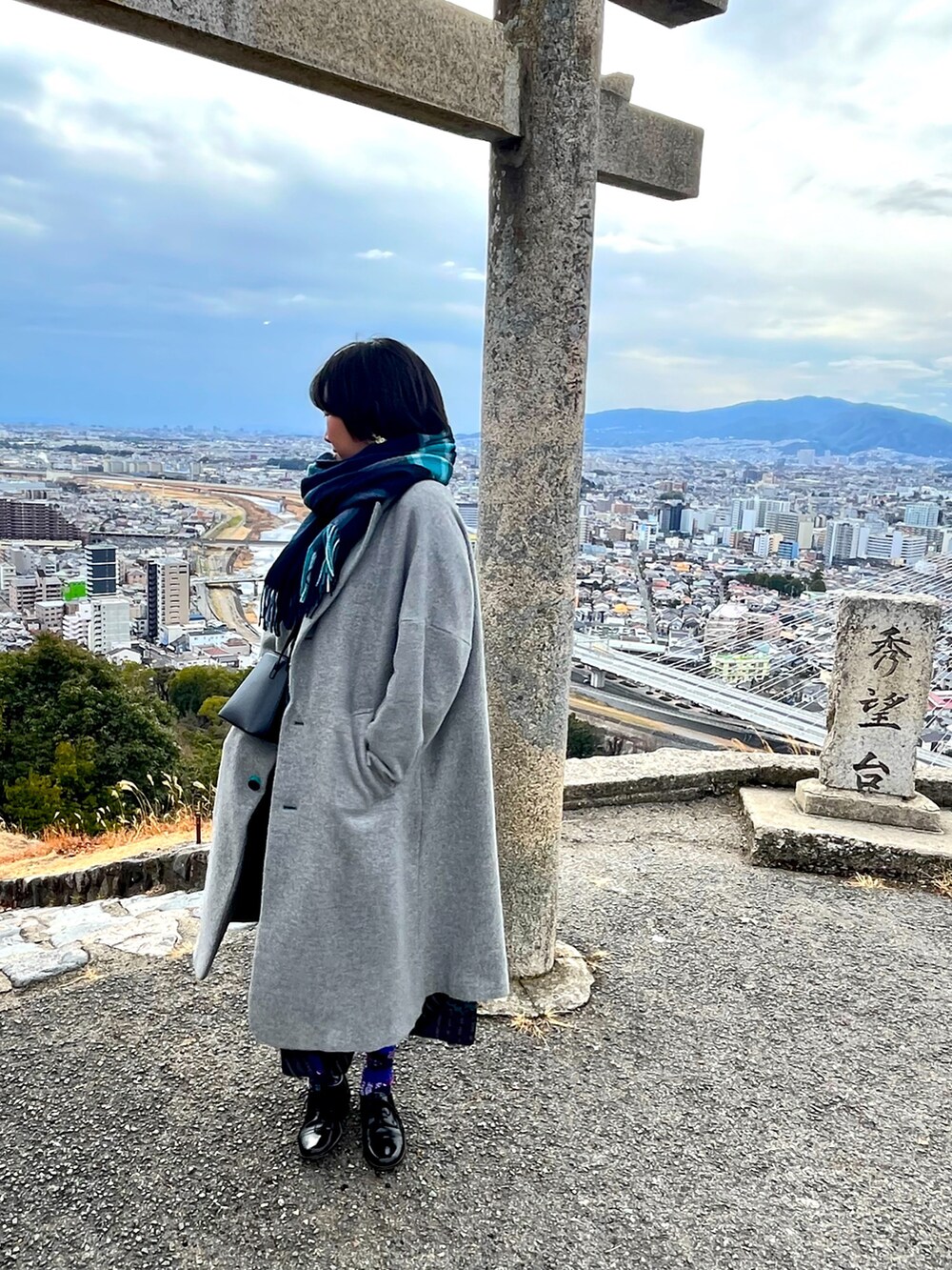 グレー系のチェスターコート、ブラック系のワンピース/ドレス、ブラック系のドレスシューズを着用したレディースの冬コーディネートの2枚目の写真