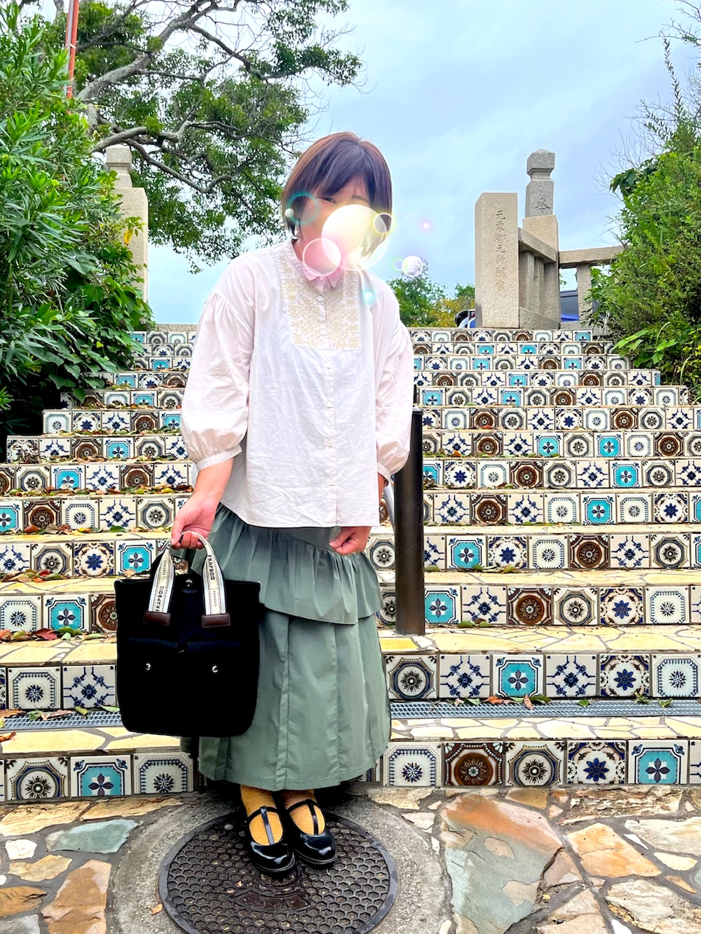 ベージュ系のシャツ/ブラウス、グリーン系のスカート、ブラック系のトートバッグを着用したレディースの冬コーディネートの2枚目の写真