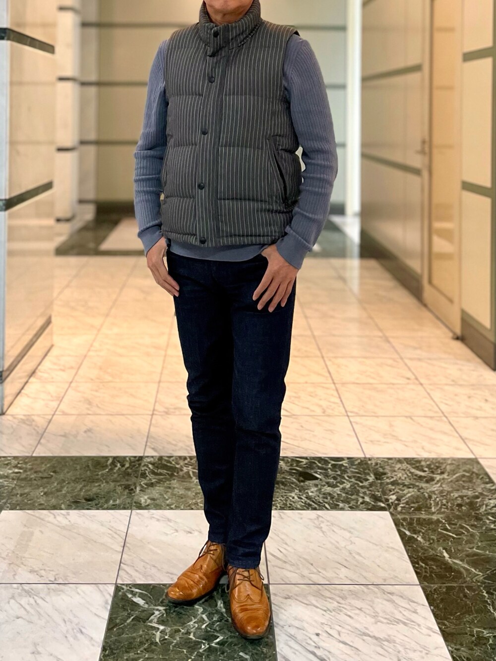 グレー系のダウンベスト、ブルー系のデニムパンツ、ブラウン系のブーツを着用したメンズの冬コーディネートの2枚目の写真