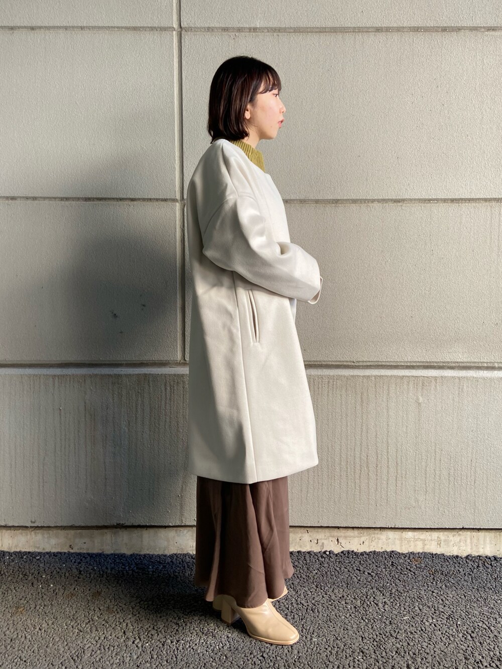 ベージュ系のその他アウター、グリーン系のニット/セーター、ブラウン系のスカートを着用したレディースの冬コーディネートの2枚目の写真