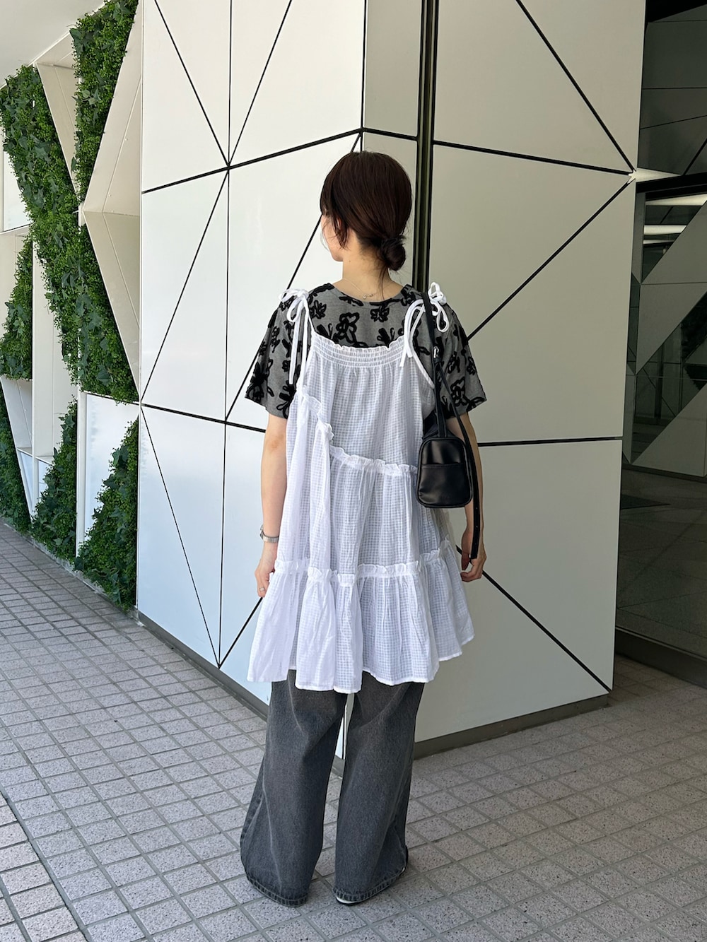 ホワイト系のチュニック、ブラック系のデニムパンツ、ブラック系のショルダーバッグを着用したレディースの夏コーディネートの3枚目の写真