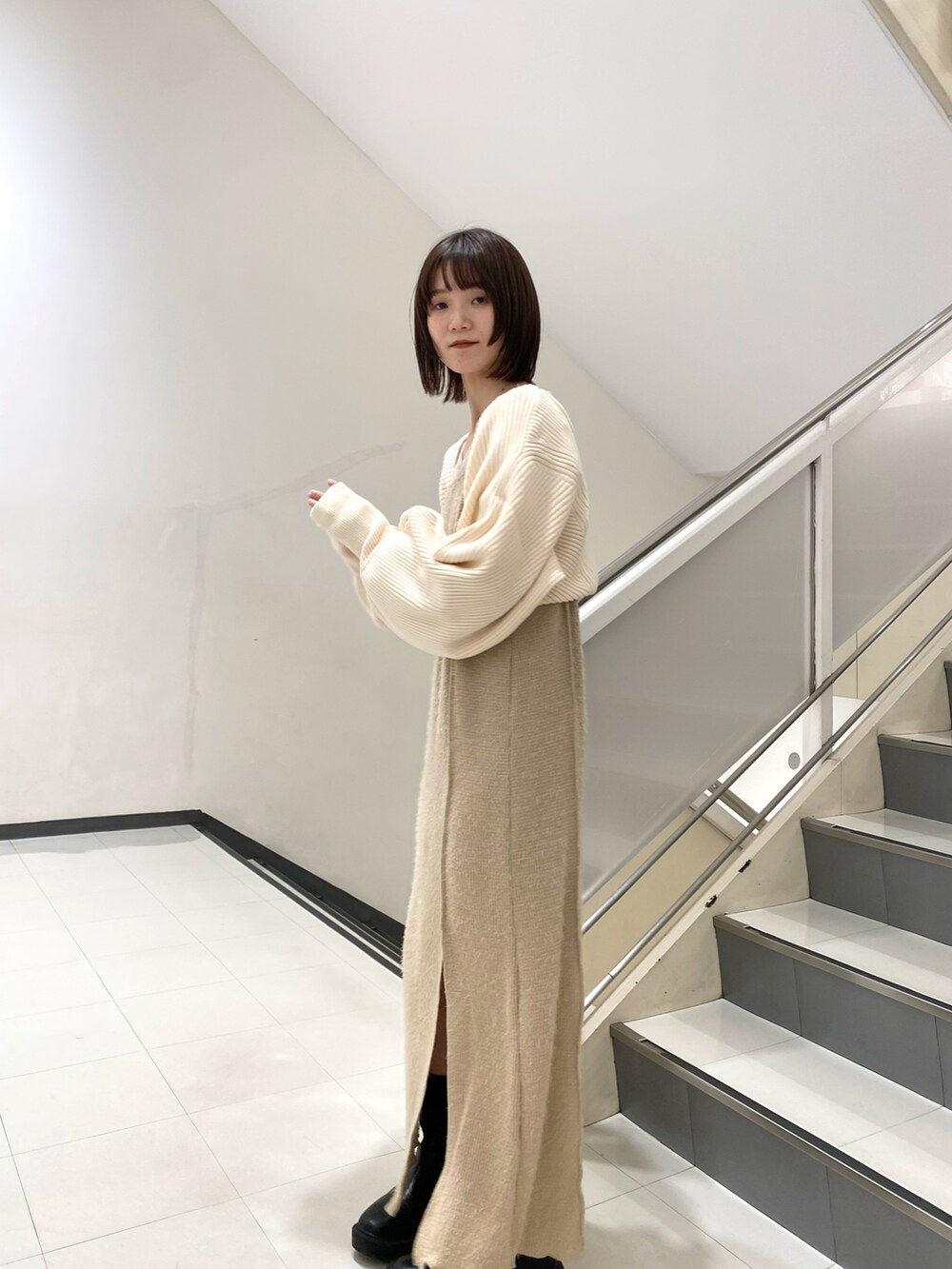 ホワイト系のカーディガン/ボレロ、ベージュ系のワンピース、ブラック系のブーツを着用したレディースの冬コーディネートの2枚目の写真