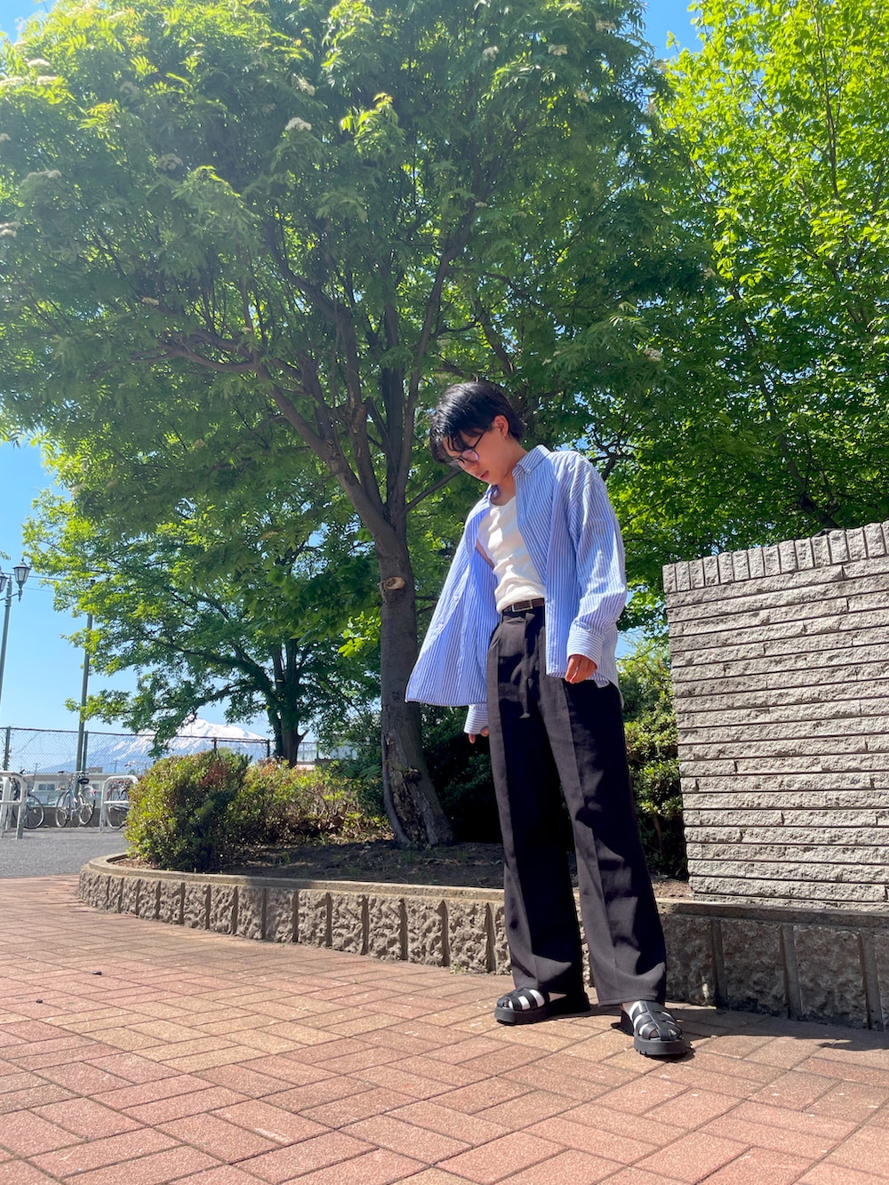ホワイト系のスラックス、ブルー系のシャツ/ブラウス、ブラック系のサンダルを着用したメンズの夏コーディネートの2枚目の写真