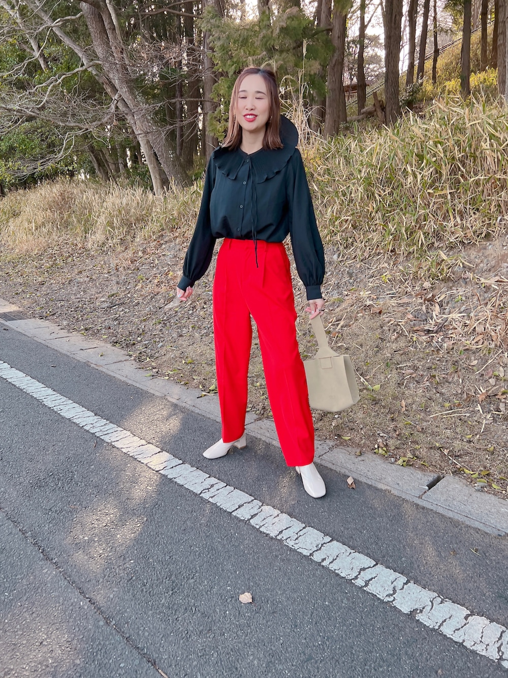 レッド系のスラックス、ホワイト系のブーツ、ベージュ系のハンドバッグを着用したレディースの春コーディネートの2枚目の写真