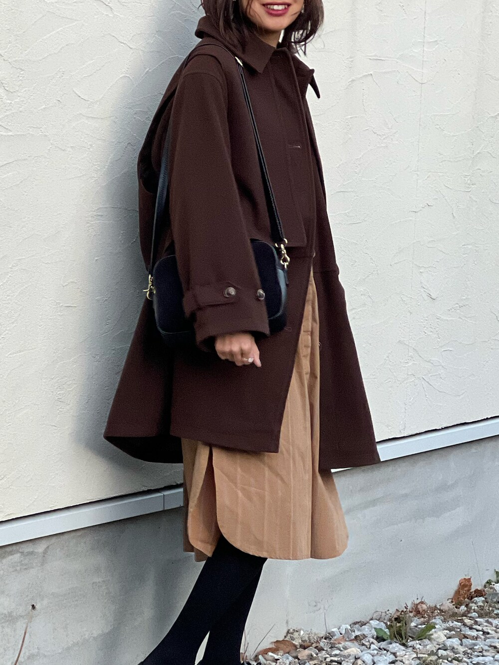 ブラウン系のステンカラーコート、イエロー系のシャツワンピース、ブラック系のショルダーバッグを着用したレディースの冬コーディネートの5枚目の写真