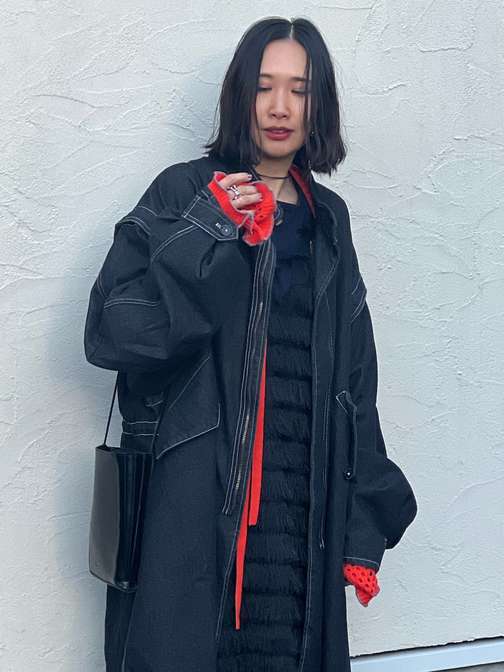 ブラック系のモッズコート、オレンジ系のカーディガン/ボレロ、ブラック系のワンピースを着用したレディースの冬コーディネートの2枚目の写真