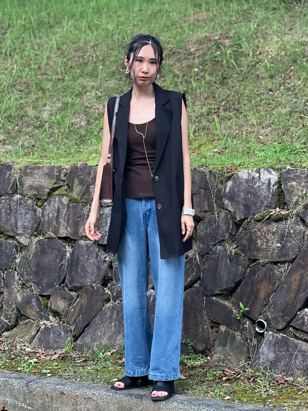 ブルー系のデニムパンツ、ブラウン系のショルダーバッグ、ブラック系のブーツを着用したレディースの夏コーディネートの3枚目の写真