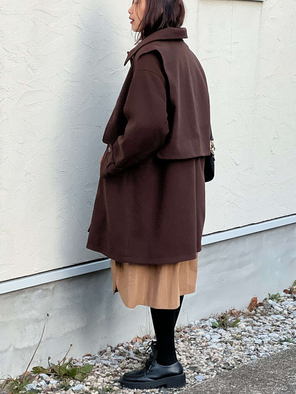 ブラウン系のステンカラーコート、イエロー系のシャツワンピース、ブラック系のショルダーバッグを着用したレディースの冬コーディネートの2枚目の写真