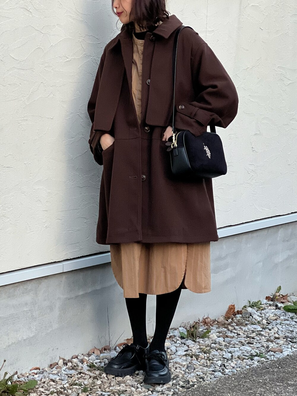 ブラウン系のステンカラーコート、イエロー系のシャツワンピース、ブラック系のショルダーバッグを着用したレディースの冬コーディネートの4枚目の写真