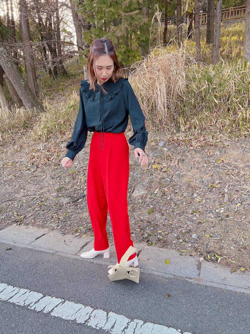 レッド系のスラックス、ホワイト系のブーツ、ベージュ系のハンドバッグを着用したレディースの春コーディネートの3枚目の写真