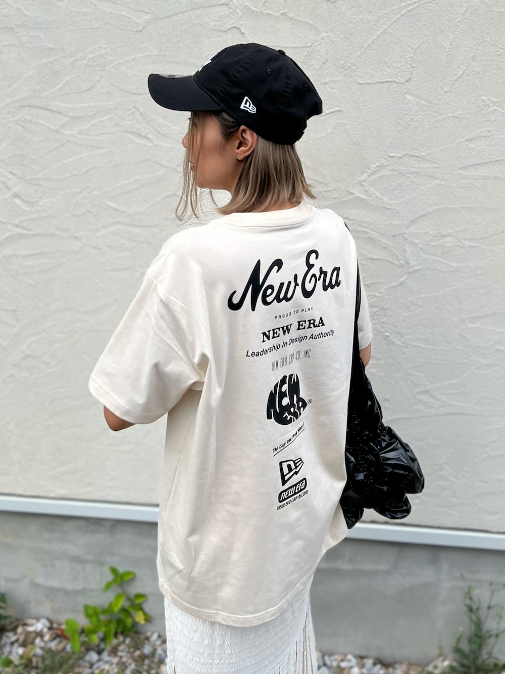 ベージュ系のTシャツ/カットソー、ブラック系のトートバッグ、ホワイト系のスカートを着用したレディースの夏コーディネートの2枚目の写真