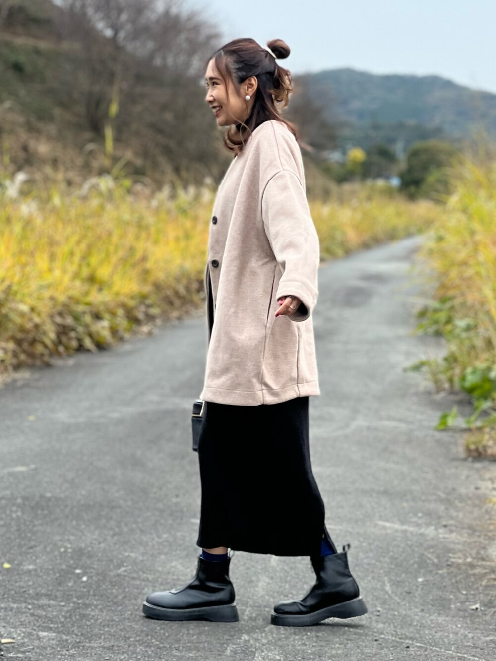 ピンク系のノーカラーコート、ブラック系のワンピース、ブラック系のブーツを着用したレディースの秋コーディネートの2枚目の写真