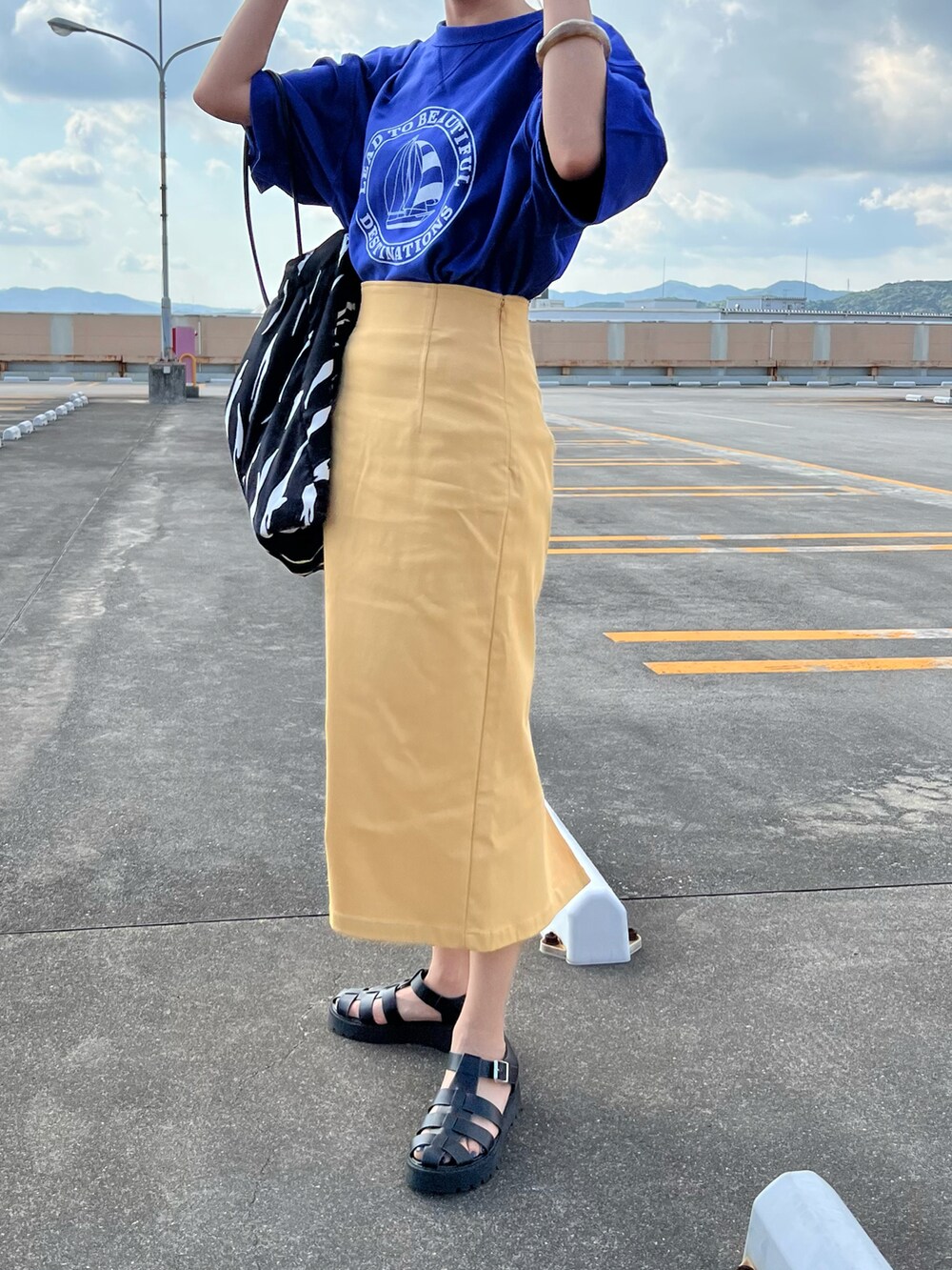 ブルー系のTシャツ/カットソー、イエロー系のスカート、ブラック系のサンダルを着用したレディースの夏コーディネートの3枚目の写真