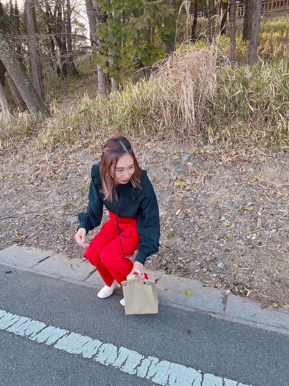 レッド系のスラックス、ホワイト系のブーツ、ベージュ系のハンドバッグを着用したレディースの春コーディネートの4枚目の写真