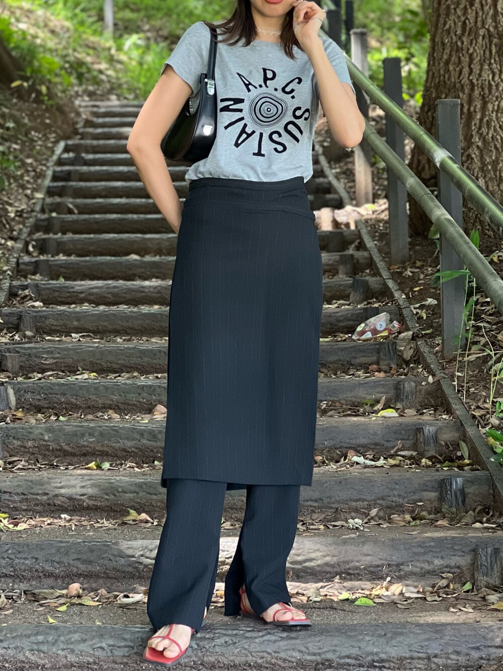 ブラック系のパンツ、ブラック系のバッグ、オレンジ系のサンダルを着用したレディースの春コーディネートの4枚目の写真