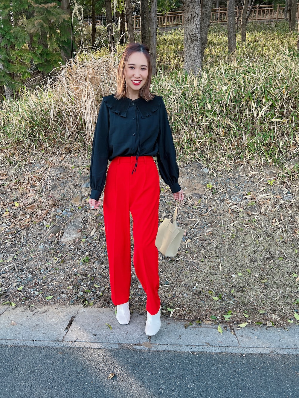 レッド系のスラックス、ホワイト系のブーツ、ベージュ系のハンドバッグを着用したレディースの春コーディネートの5枚目の写真