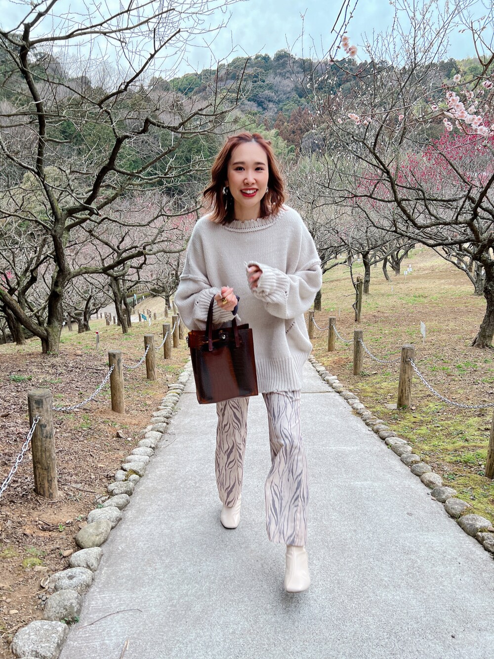 グレー系のニット/セーター、ホワイト系のブーツ、ブラウン系のトートバッグを着用したレディースの春コーディネートの3枚目の写真