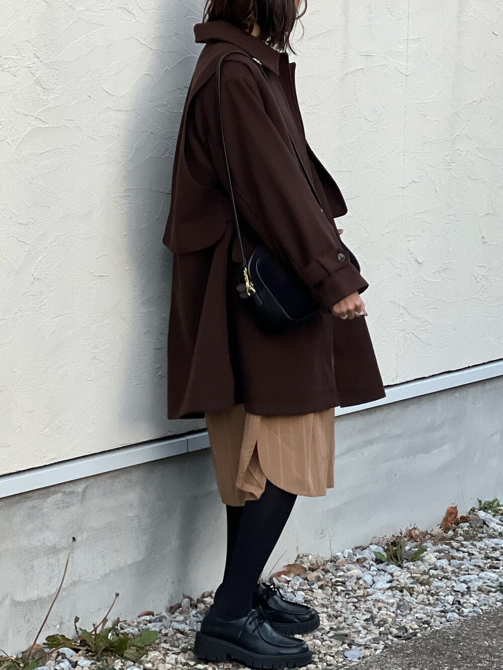 ブラウン系のステンカラーコート、イエロー系のシャツワンピース、ブラック系のショルダーバッグを着用したレディースの冬コーディネートの3枚目の写真