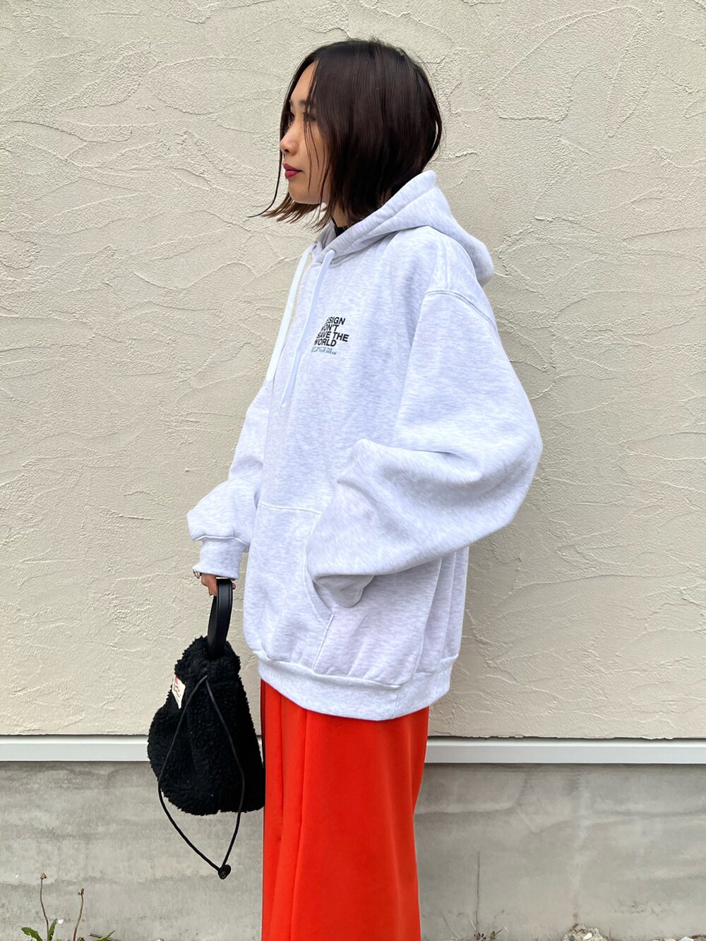 グレー系のパーカー、オレンジ系のスカート、シルバー系のスニーカーを着用したレディースの秋コーディネートの3枚目の写真